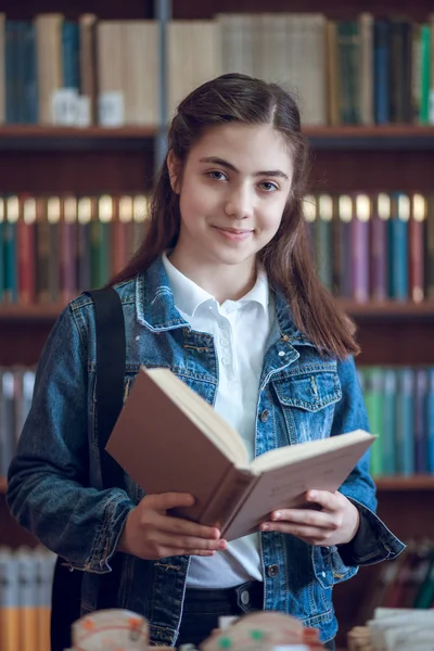 Belle écolière dans la bibliothèque lisant un livre — Photo