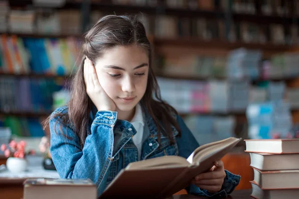 Bela estudante sentada na biblioteca e lendo um livro — Fotografia de Stock