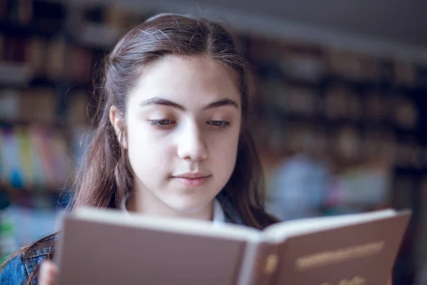 Belle écolière dans la bibliothèque lisant un livre — Photo