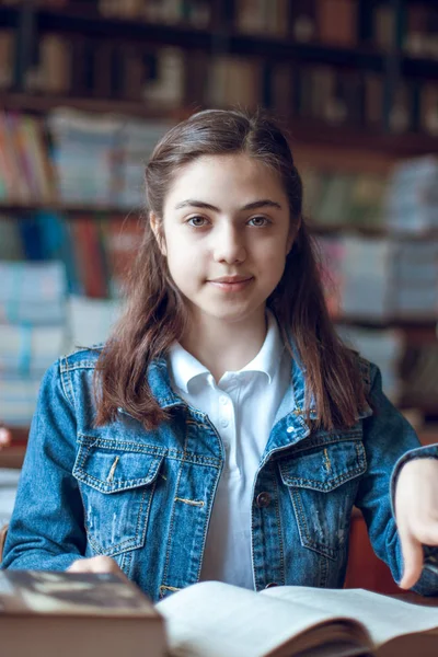 Bela estudante sentada na biblioteca e lendo um livro — Fotografia de Stock