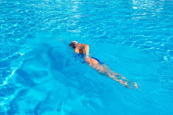 Mujer con traje de baño nadando en una piscina de agua azul. — Foto de Stock