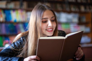 Güzel genç kız öğrenci kütüphanede oturan ve okuma