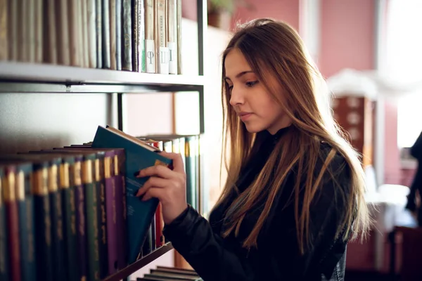 Bela adolescente estudante lendo um livro na biblioteca — Fotografia de Stock