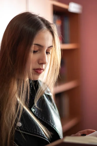 Bela adolescente estudante lendo um livro na biblioteca — Fotografia de Stock