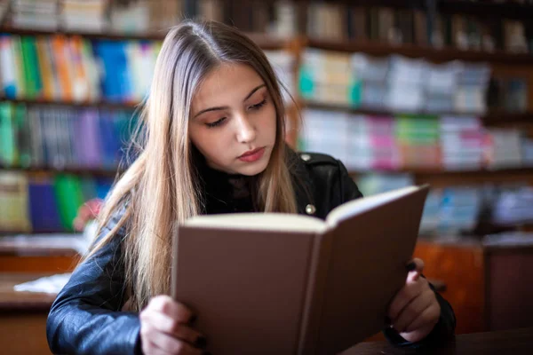 Hermosa adolescente colegiala sentada en la biblioteca y leyendo — Foto de Stock