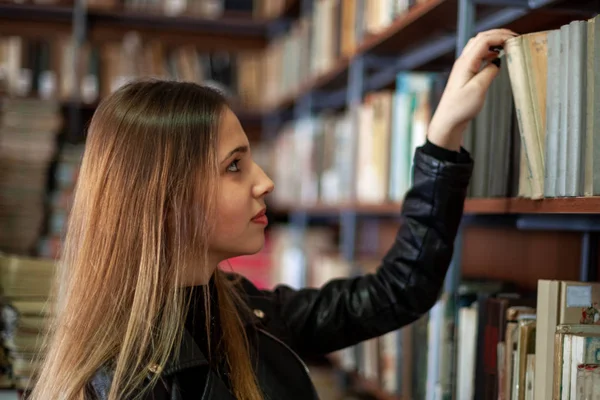 Bela adolescente estudante escolhendo um livro na biblioteca — Fotografia de Stock