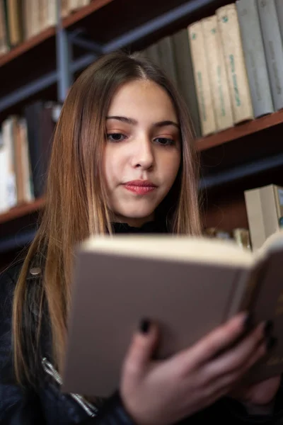 Bela adolescente estudante lendo um livro na biblioteca — Fotografia de Stock