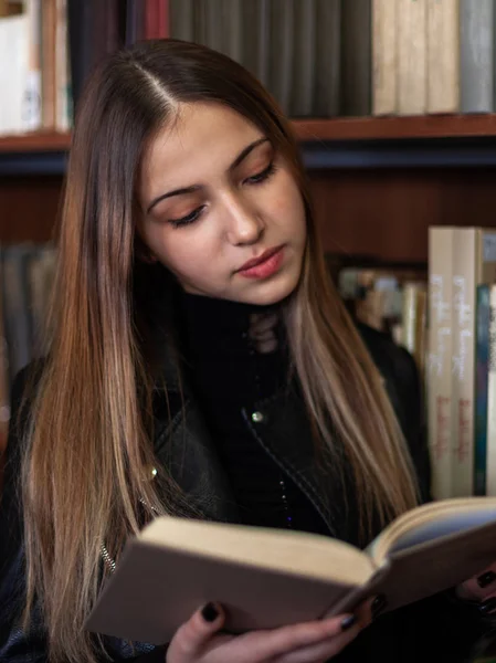 Bela adolescente estudante lendo um livro na biblioteca — Fotografia de Stock