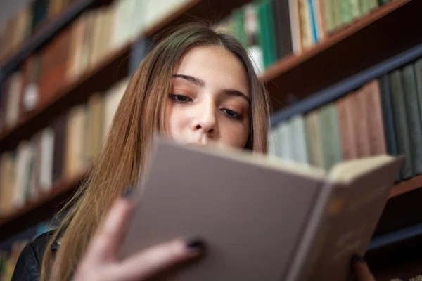 Bela adolescente estudante lendo um livro na biblioteca — Fotografia de Stock