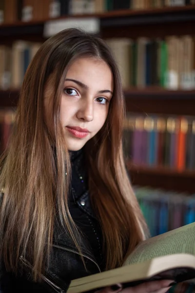 Bela adolescente estudante lendo um livro na biblioteca — Fotografia de Stock