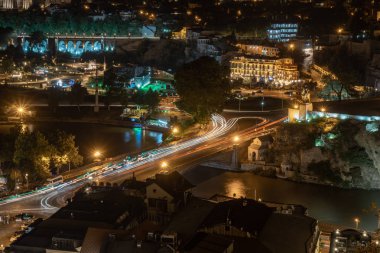 Tiflis Metekhi köprüsü boyunca araba ışıkları, Gürcistan, gece. Avrupa meydanı, Kura nehri kıyısı. Seyahat.