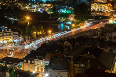 Tiflis Metekhi köprüsü boyunca araba ışıkları, Gürcistan, gece. Avrupa meydanı, Kura nehri kıyısı. Seyahat.