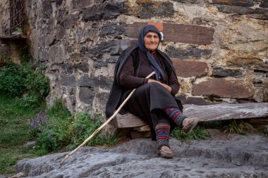 Ushguli, Gürcistan - 09.08.2019: Yaşlı kadın önünde oturuyor