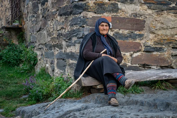 Ushguli, Gürcistan - 09.08.2019: Yaşlı kadın önünde oturuyor