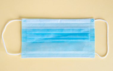 Sarı arka planda izole edilmiş tıbbi koruyucu maske, koronavirüsü önle