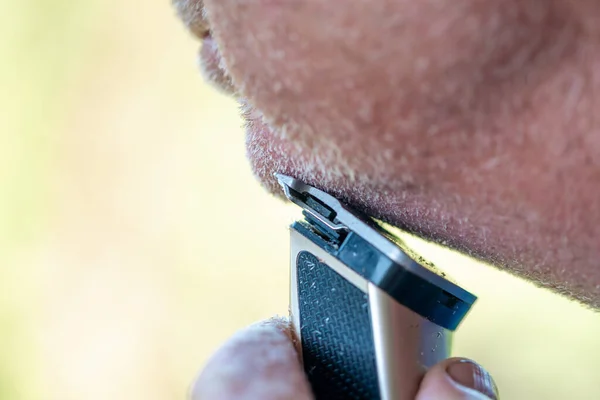 A man cuts his white beard with a clipper, people