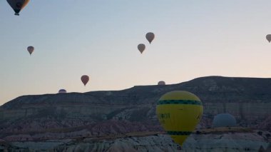 Kapadokya, Türkiye - 5 Ağustos 2025: Kapadokya 'da gündoğumunda kayalık arazide uçan sıcak hava balonu. Seyahat