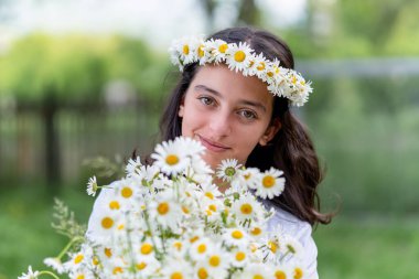 Kafasında papatya çelengi ve ellerinde papatya buketi olan tatlı bir genç kız. Portre