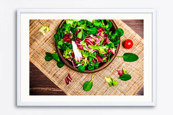 Provence salad. Leaves of endive or chicory, lamb and rose salad. Cherry tomato. Raw vegetables. On wooden table. Wall frame poster with leaf salad photo. Mockup template.