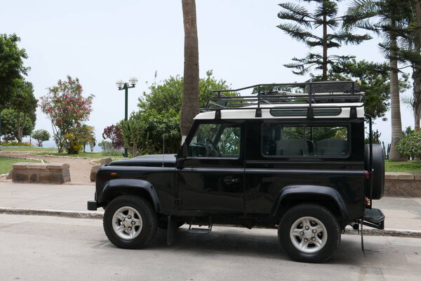 Лима, Перу. 27 декабря 2017 года. Спереди и сбоку вид мятного состояния черный Land Rover Defender с белым верхом. Автомобиль припаркован на улице Barranco района Лима вдоль стороны общественного парка
.  