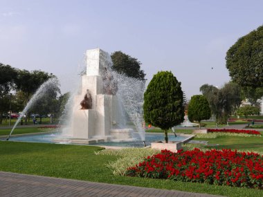 Doğal gün görünümünü waterjet çeşmeden mavi gökyüzü gün sihirli su devresi Lima rezerv Park. Görüntünün içinde çiçekler, bir çim, bir yaya yolu, arızi insanlar, ağaçlar ve inşa inşaat süs bahçeleri vardır