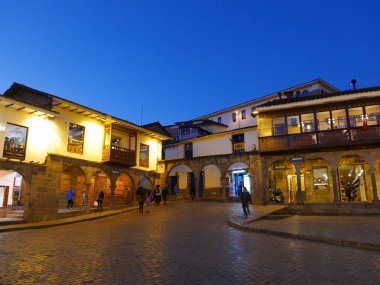 Cusco ana kare veya Plaza de Armas, mavi gökyüzü, arızi kişi, kemerler ve taş zemine etrafında ışıklı konut gelişiminin doğal gece görünümü. 