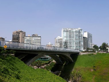 Villena köprü Lima Miraflores bölgesinde doğal görünümünü. Resimdeki avuç içi, ağaçlar, çim, bitkiler, çiçek, bir park, sokak, dış modern binalar ve bir uçurumun üzerinde bir güzel ve mavi gökyüzü gün vardır.