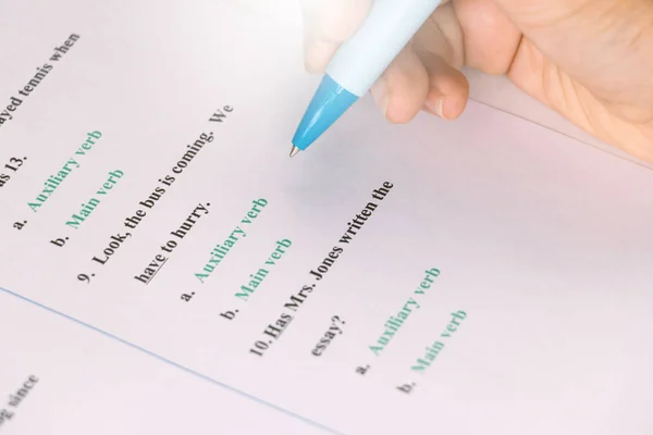 stock image student's hand holding blue pen taking English test on white desk in class