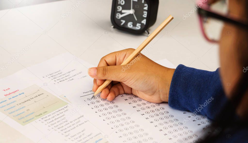 student's hand holding blue pen taking English test on white desk in class