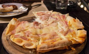 Akşam lokantada, ahşap tabakta taze, sulu pastırmalı pizza.