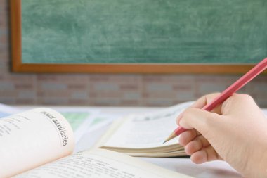 Sınıfta karatahtanın önündeki masanın üzerindeki bulanık ders kitabı üzerinde el ele tutuşmak.