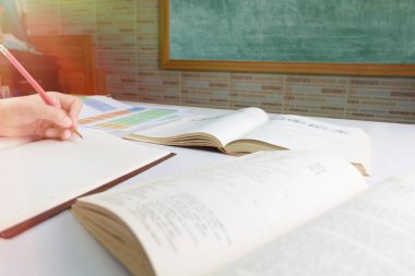 Sınıfta karatahtanın önündeki masanın üzerindeki bulanık ders kitabı üzerinde el ele tutuşmak.