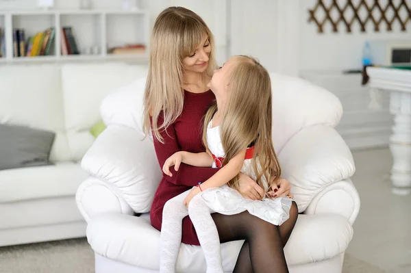 Beautiful mother and daughter are sitting on a white armchair.