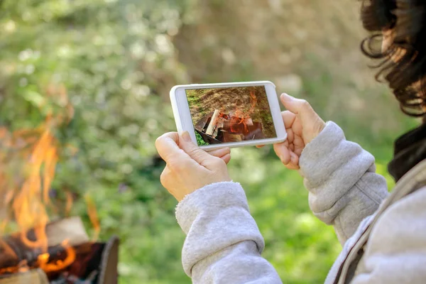 Kadın resimleri ateş üstünde onun smartphone alıyor. Açık havada. Yakın çekim.