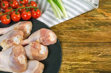 Çiğ tavuk sopaları, kırmızı domates ve yeşil soğan ahşap arka plan üzerinde siyah bir tabak yalan. Pişirme kavramı. Metin için yer kopyalayın. Yakın çekim.