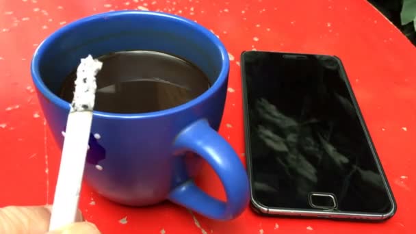 一杯咖啡和一台智能手机在一个红色的 划伤的办公桌上 上面有一阴香烟 — 图库视频影像