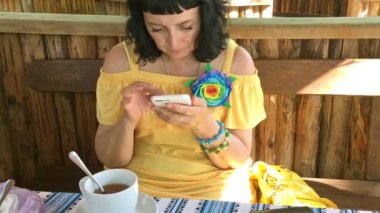 Sarı giysili kadın sokak kafe masada çay içme ve onun smartphone kullanarak. Yakın çekim.
