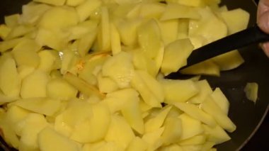Patates dilimleme yağda kızartılmış. Bir tavada kızartılmış patates, siyah mutfak spatula ile karıştırılır. Yakın çekim.