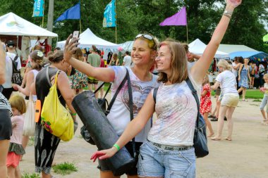 Kiev, Ukraine, July 2018: - Two girls are photographed using a smartphone on a street event. Outdoors. clipart