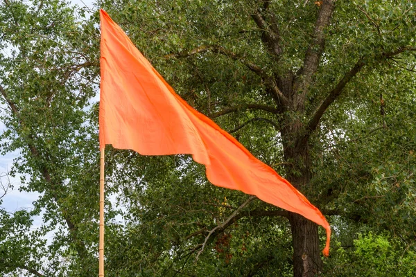 Orange flag flutters in the wind against the background of the trees. Outdoors.