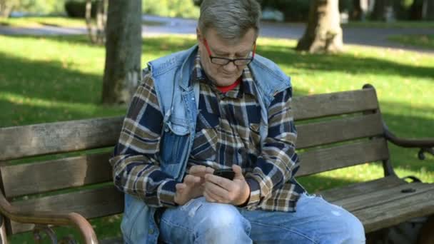 Ein Älterer Mann Freizeitkleidung Und Brille Sitzt Auf Einer Parkbank — Stockvideo