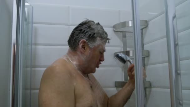 バスルームのインテリア 大人の白人の民族の男はシャワーを取り マイクに向かって歌うふりをします モダンなシャワー 浴室で水をはね — ストック動画