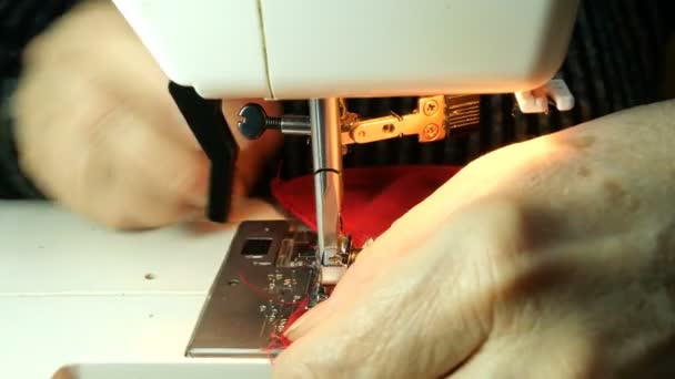 仕立て作業のプロセス 高齢者女性の裁縫師の手は 赤い布の服を縫う針 ルーパーとミシンの押え 小さなホーム ビジネス コンセプト — ストック動画