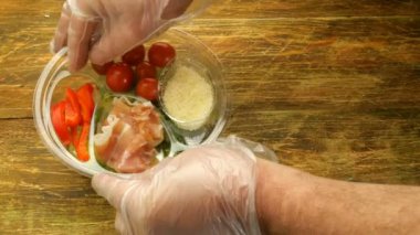 Şeffaf bir kapsayıcı sağlıklı fast food. Domates, biber, jamon ve marul ile hızlı yemek pişirmek için sebze salatası. Tek kullanımlık eldiven insan elinde hazırlamak.
