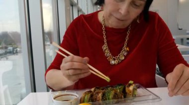 Kadın bir restoran ya da suşi barda tahta çubukla wasabi, zencefil ve soya sosu ile suşi yiyor. Yakın çekim. Eller parçası.
