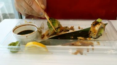 Kadın bir restoran ya da suşi barda tahta çubukla wasabi, zencefil ve soya sosu ile suşi yiyor. Yakın çekim. Eller parçası.