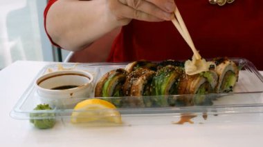 Kadın bir restoran ya da suşi barda tahta çubukla wasabi, zencefil ve soya sosu ile suşi yiyor. Yakın çekim. Eller parçası.