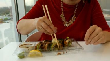 Kadın bir restoran ya da suşi barda tahta çubukla wasabi, zencefil ve soya sosu ile suşi yiyor. Yakın çekim. Eller parçası.