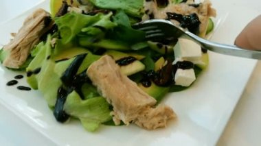 Beyaz bir tabak içinde bir çatal ile tuna, sebze, marul ve peynir salatası karışık. Yakın çekim.