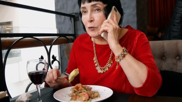 レストランやカフェで上品な年配の女性はワインを飲むと 彼女のスマート フォンで話して サラダを食べています — ストック動画